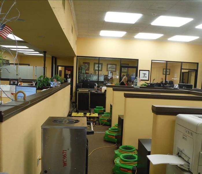 A commercial office with cubicles flooded with water. At least six pieces of equipment are present to dry the damages. 