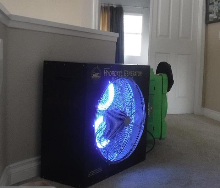 A machine that looks like a large square fan glowing blue in the center is used to professionally remove odors