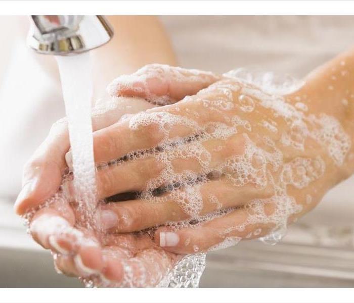 A close-up view of a sink water faucet pouring freshwater over a pair of soapy sudsed up hands