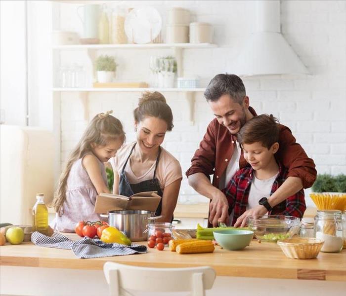 A happy family is in their clean kitchen cooking together. An assortment of healthy whole foods are being prepared
