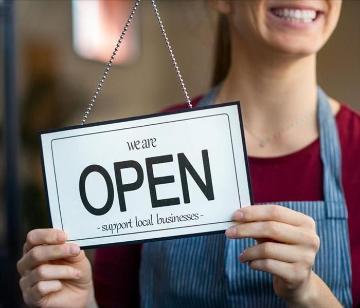 A smiling Shop owner turns the closed sign to OPEN