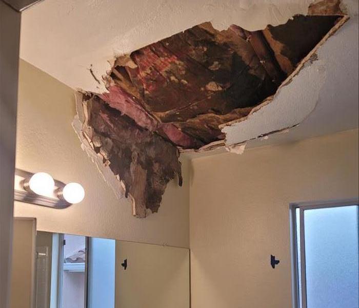 A bathroom shows water damage to the ceiling when rain soaked materials became too heavy and fell