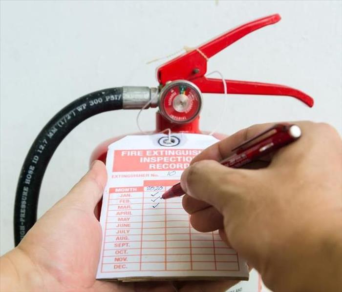 A close up of a fire extinguisher and its tag log. A man is checking off for maintenance purposes