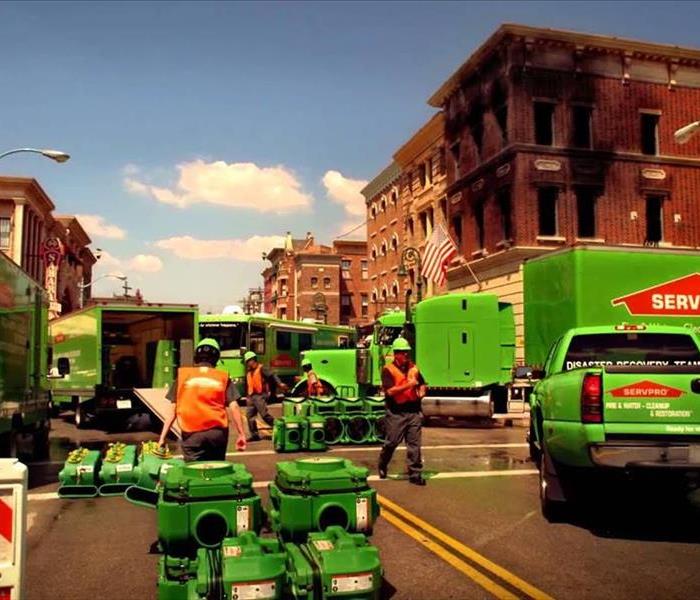 At a city intersection with a burned brick building, SERVPRO professionals are unloading equipment to start restoration