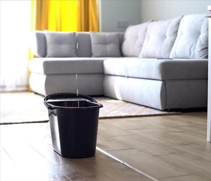 A family room has a bucket in the middle of the floor to catch the stream of dripping water from the ceiling