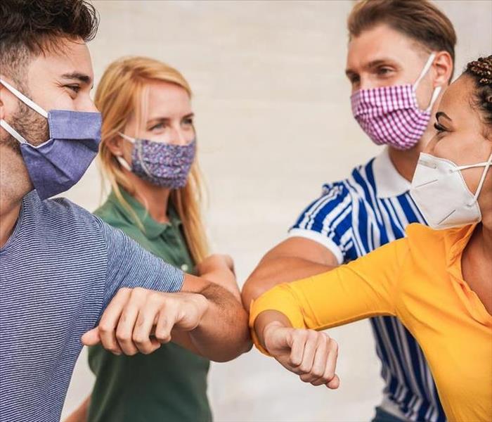 Four friends wearing masks, elbow bump as a group instead of hugging as a greeting to stay safe from the virus 