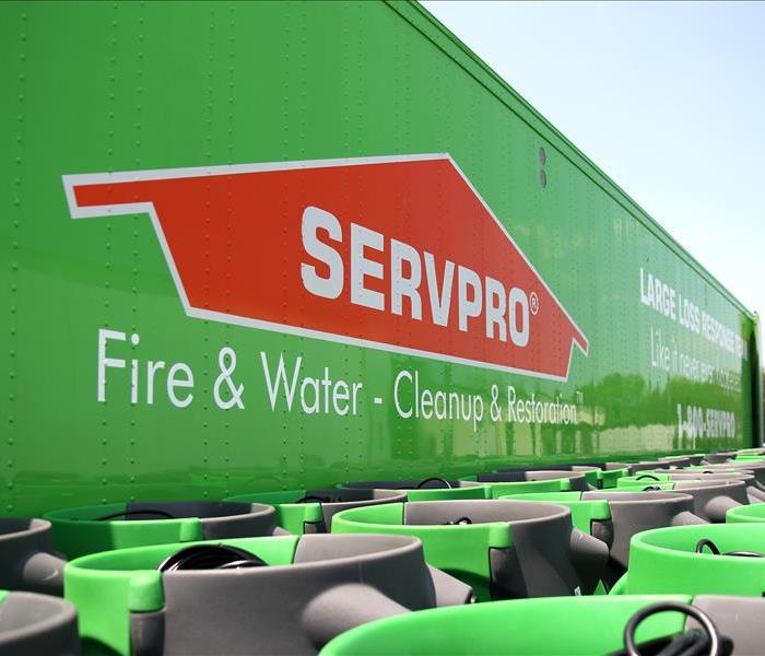 A bright lime green super long SERVPRO semi-tractor trailer parked with endless stacks of bright green specialty equipment