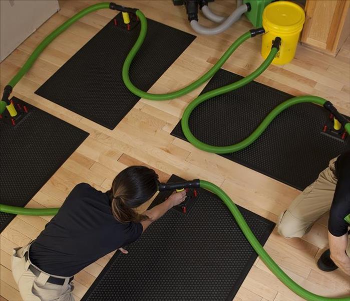Two techs are setting up large mats to dry by use of hot air to remove moisture, to save the wood floors.
