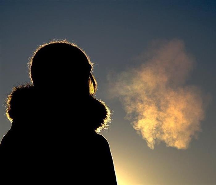 A clear blue sky with the silhouette of  the back of a woman in a coat. Perhaps she is pondering or appreciating her view 