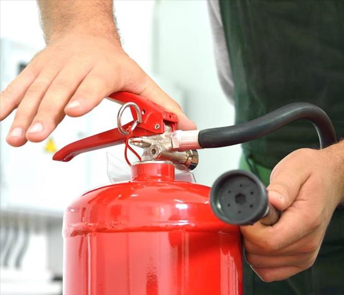 A kitchen worker wearing an apron reaches for a a bright red fire extinguisher to put into use