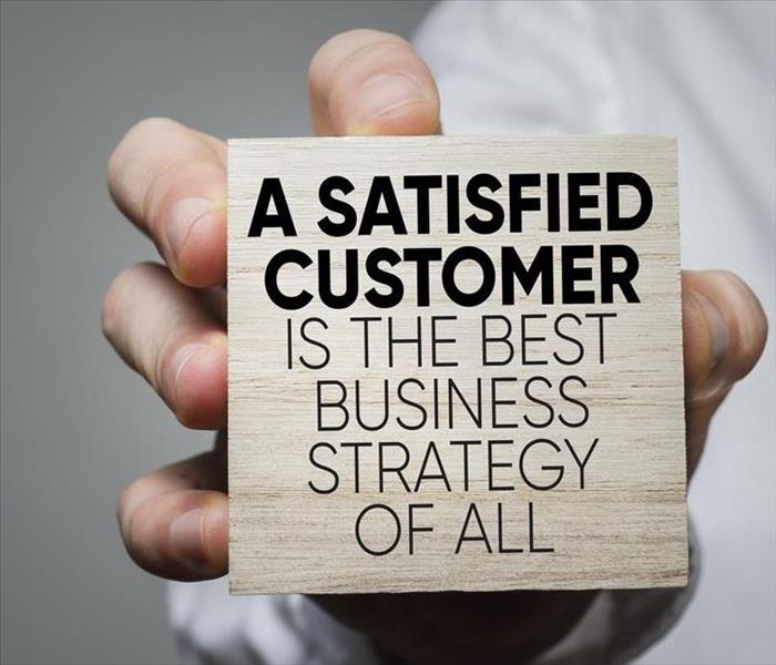 A close up of a man holding a square wood block that in black bold letters says: A Satisfied Customer is the best of all