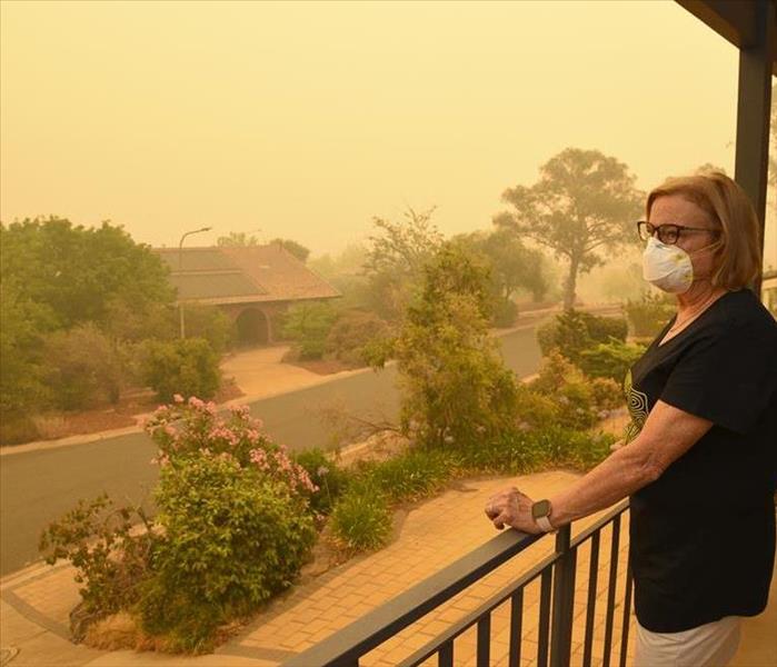 A woman wearing an N95 mask looks out on her balcony as her neighborhood fills with smoke from a nearby brush or wildfire