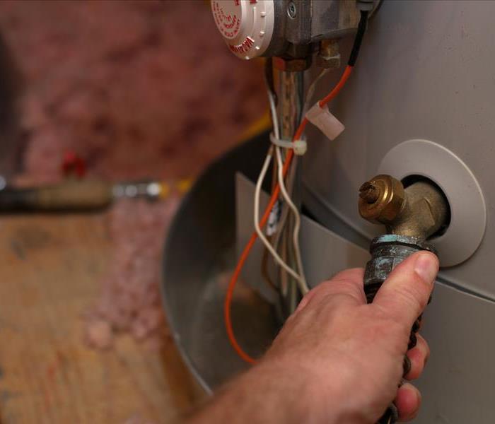 At the base of a home water heater, a firm hand is ensuring the valve is tight and secure