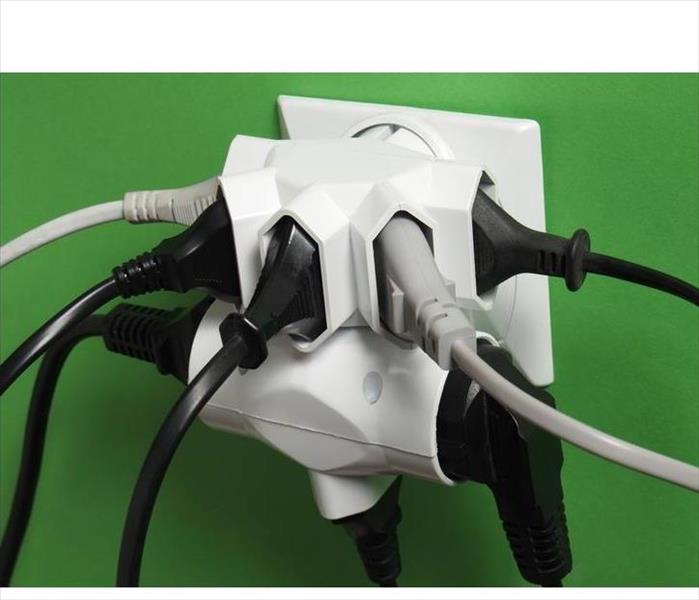 A wall electrical outlet has an adapter converter for multiple plugs. Everyone of the eight have a plugged in cord. DANGER!